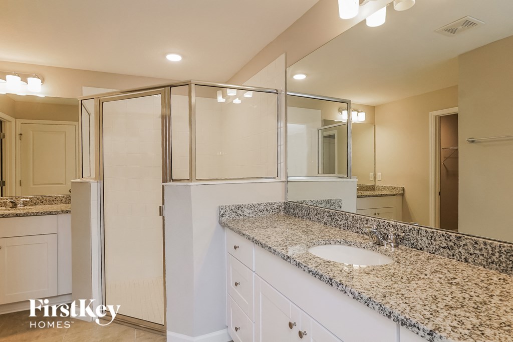 a bathroom with white cabinets and granite counter tops and a shower