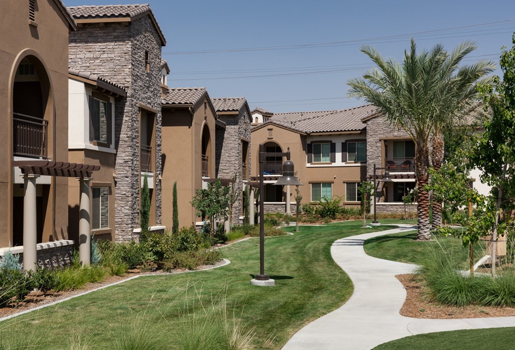 a walkway between two apartment buildings with grass and palm trees