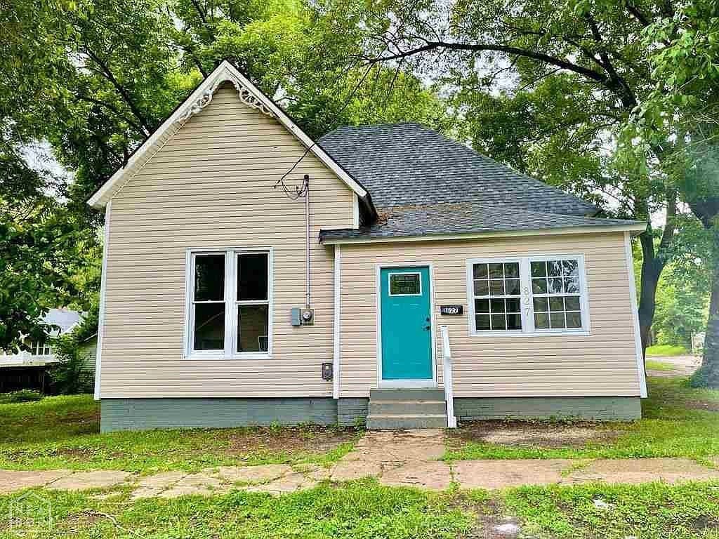 A small house with a blue door is surrounded by trees.