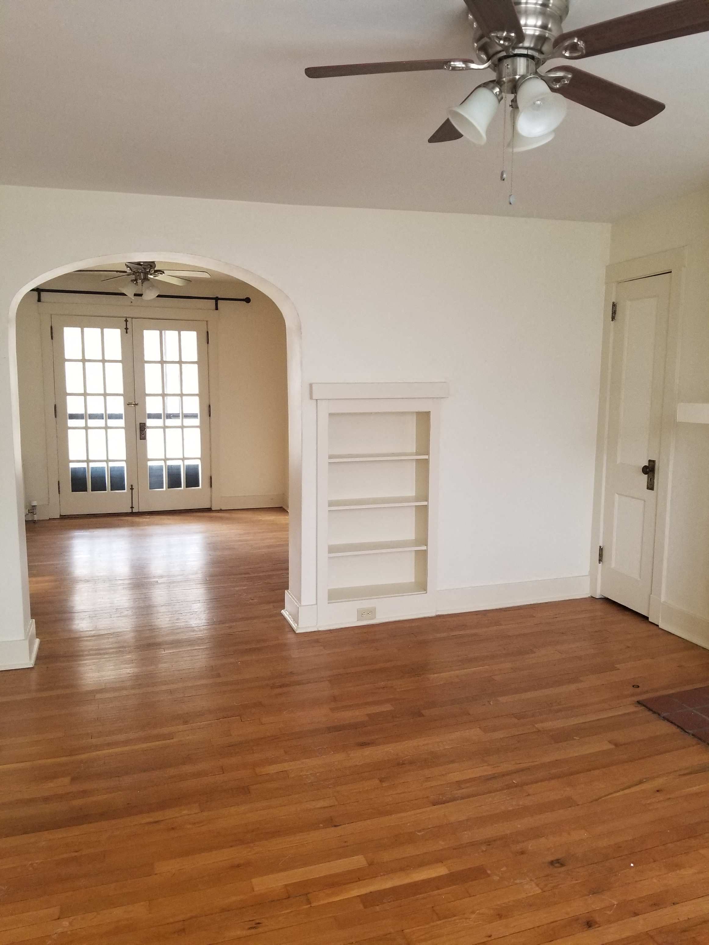 an empty living room with a wooden floor and a ceiling fan