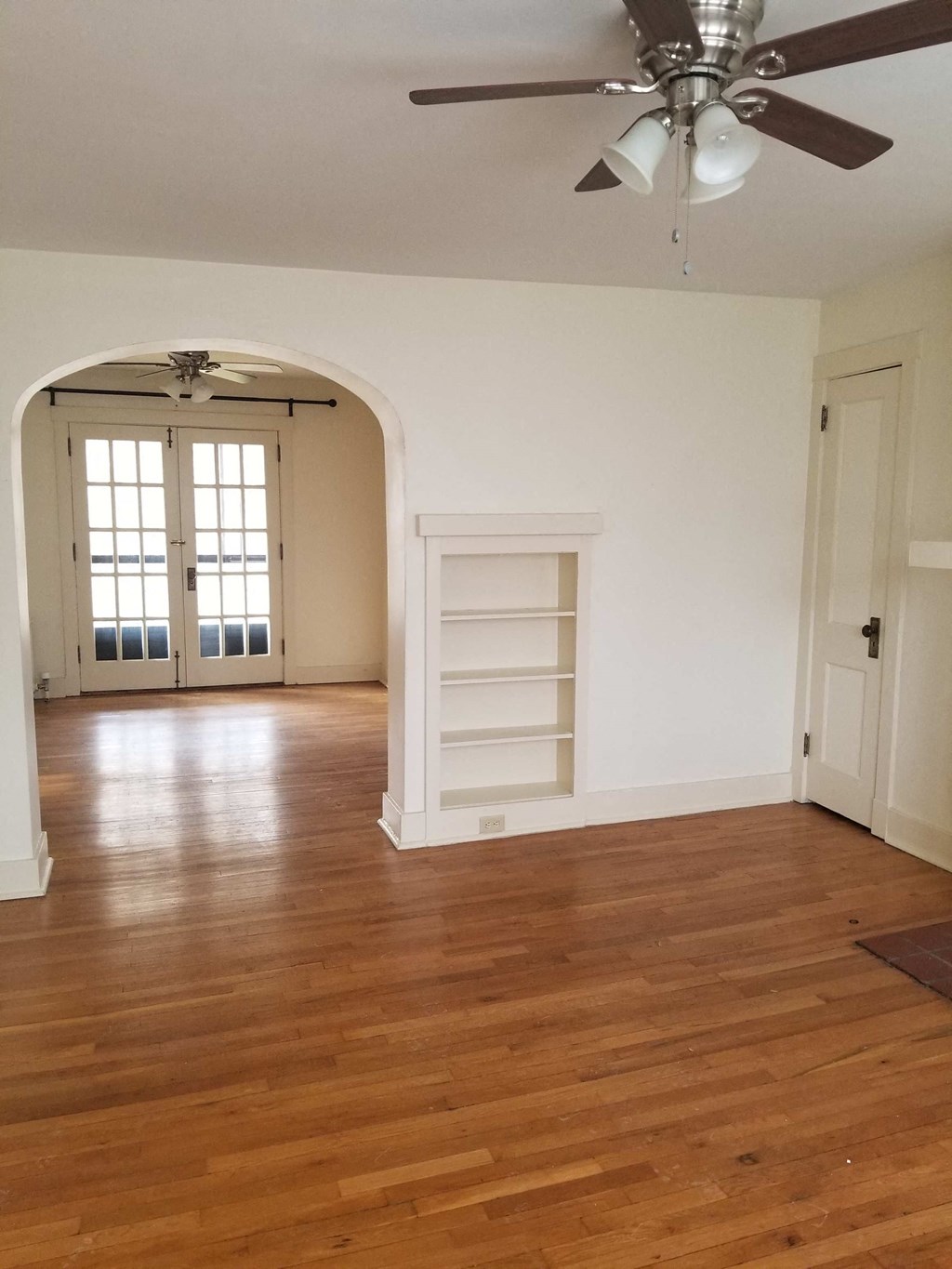 an empty living room with a wooden floor and a ceiling fan