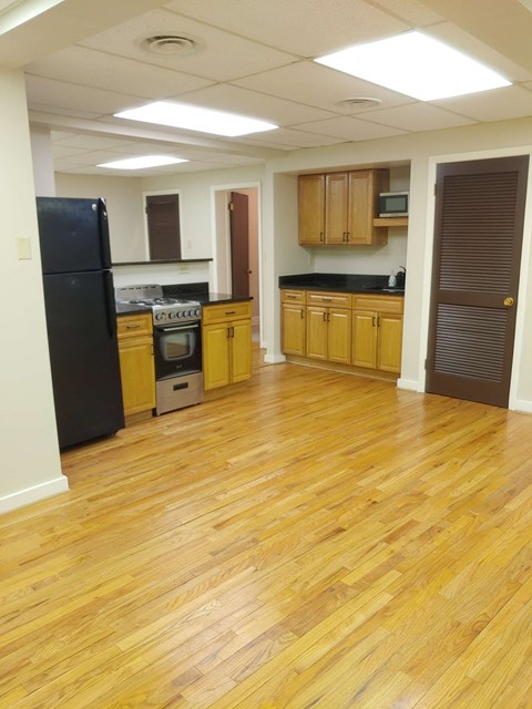 an empty kitchen with wooden floors and a black refrigerator