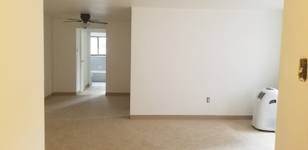 an empty living room with a white wall and a ceiling fan