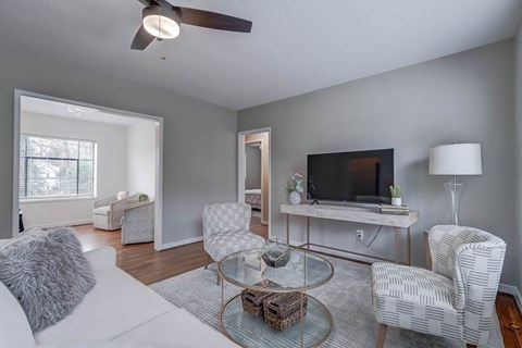 A living room with a white couch, a glass coffee table, and a television on a stand.