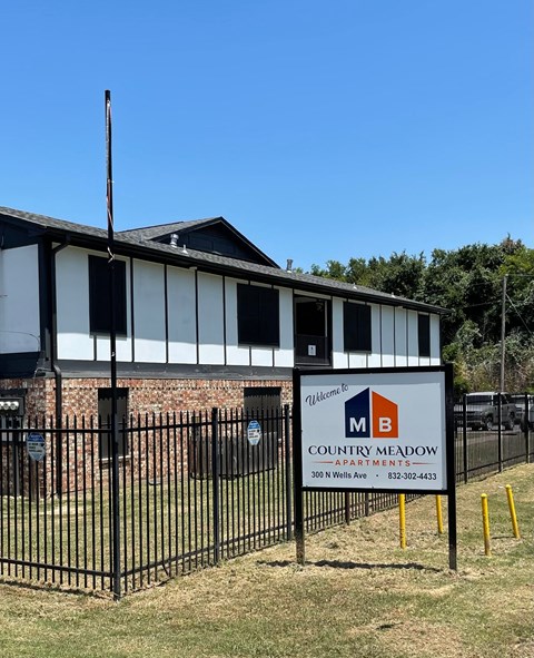 A sign for Country Meadow Apartments is displayed in front of a brick building.