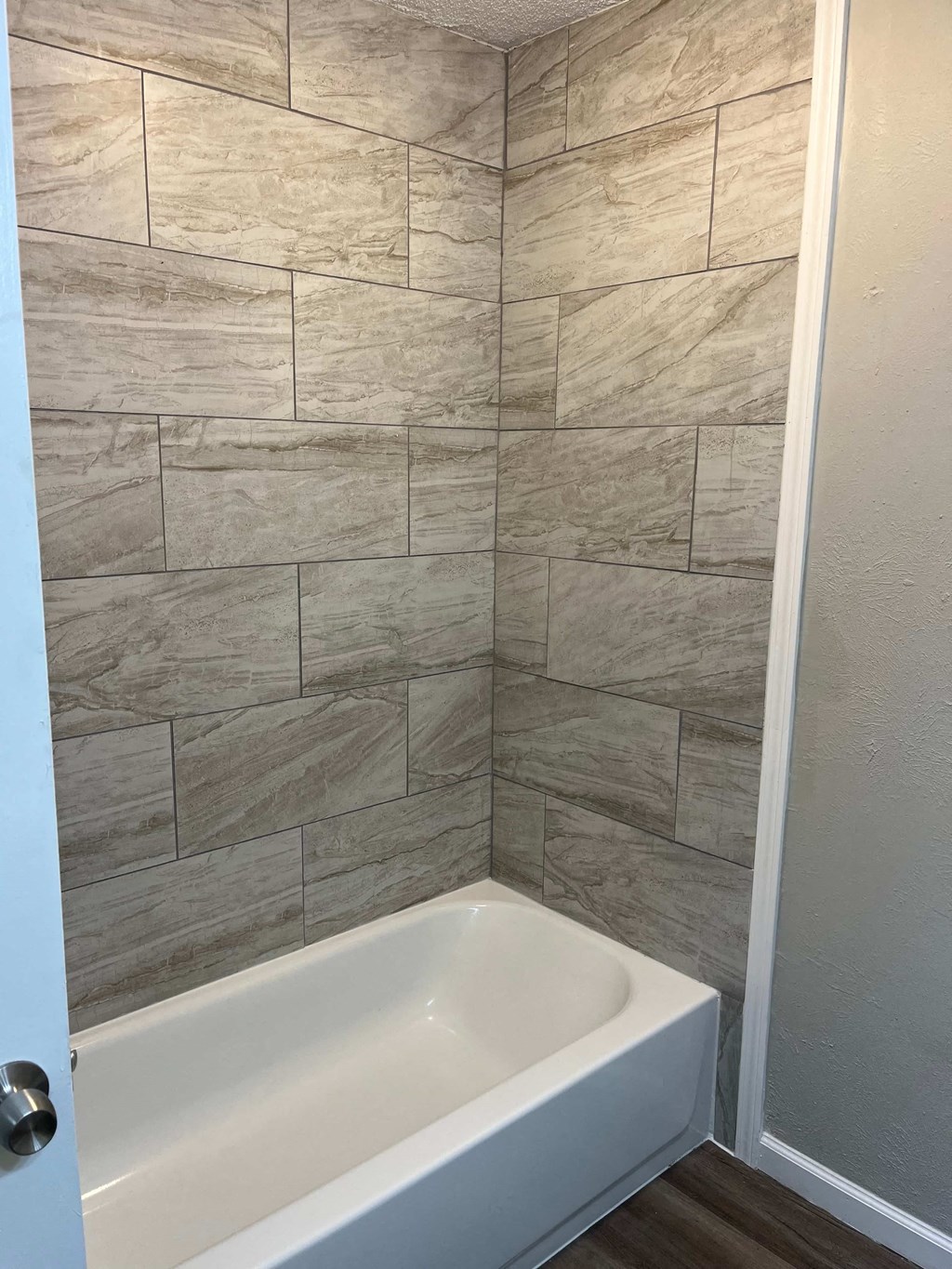 A white bathtub sits in a bathroom with a tiled wall.