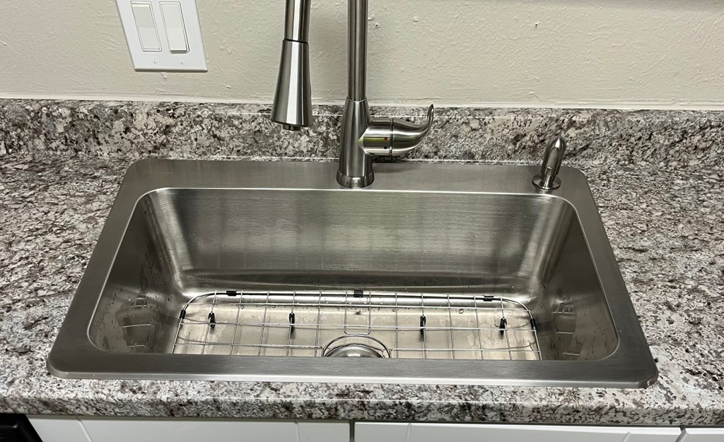 A stainless steel kitchen sink with a faucet and a drain grid.