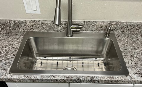 A stainless steel kitchen sink with a faucet and a drain grid.
