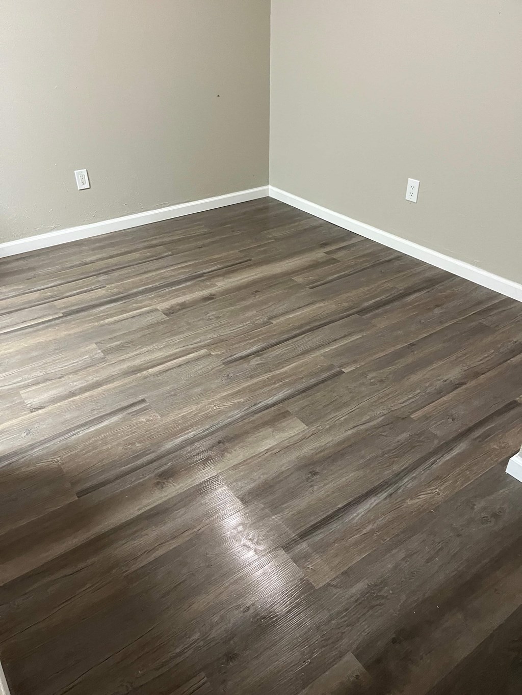 A room with a wooden floor and two switches on the wall.