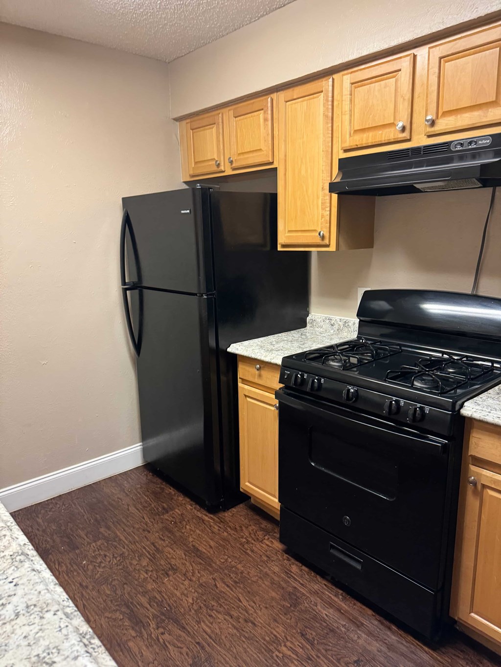 A black fridge and stove in a kitchen with wooden cabinets.