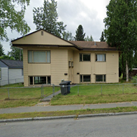 A tan house with a black trash can in front of it.