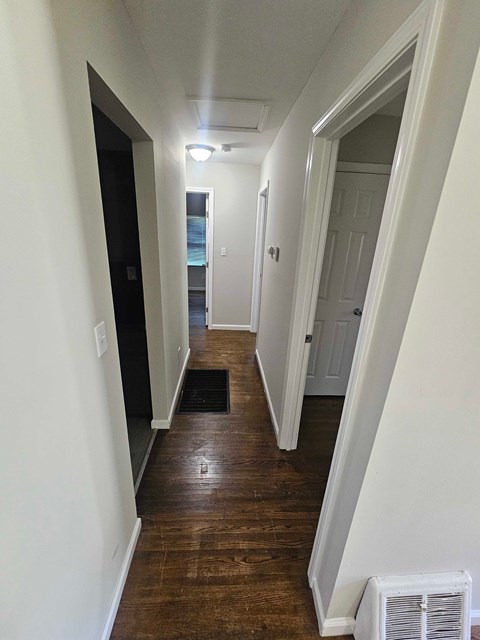 A long hallway with a white wall and a black door.