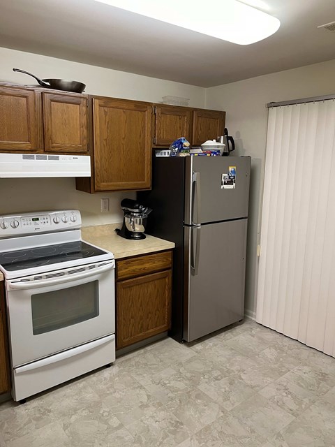 A kitchen with a white stove top oven, a white dishwasher, a white refrigerator, and wooden cabinets.