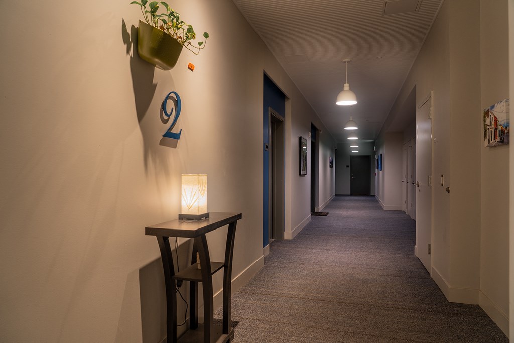 a long hallway with a table and a lamp and a door number on the wall