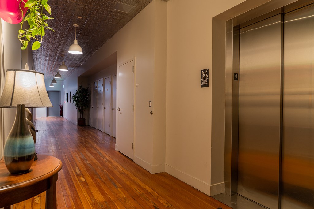 a hallway with wooden floors and stainless steel elevators and a lamp
