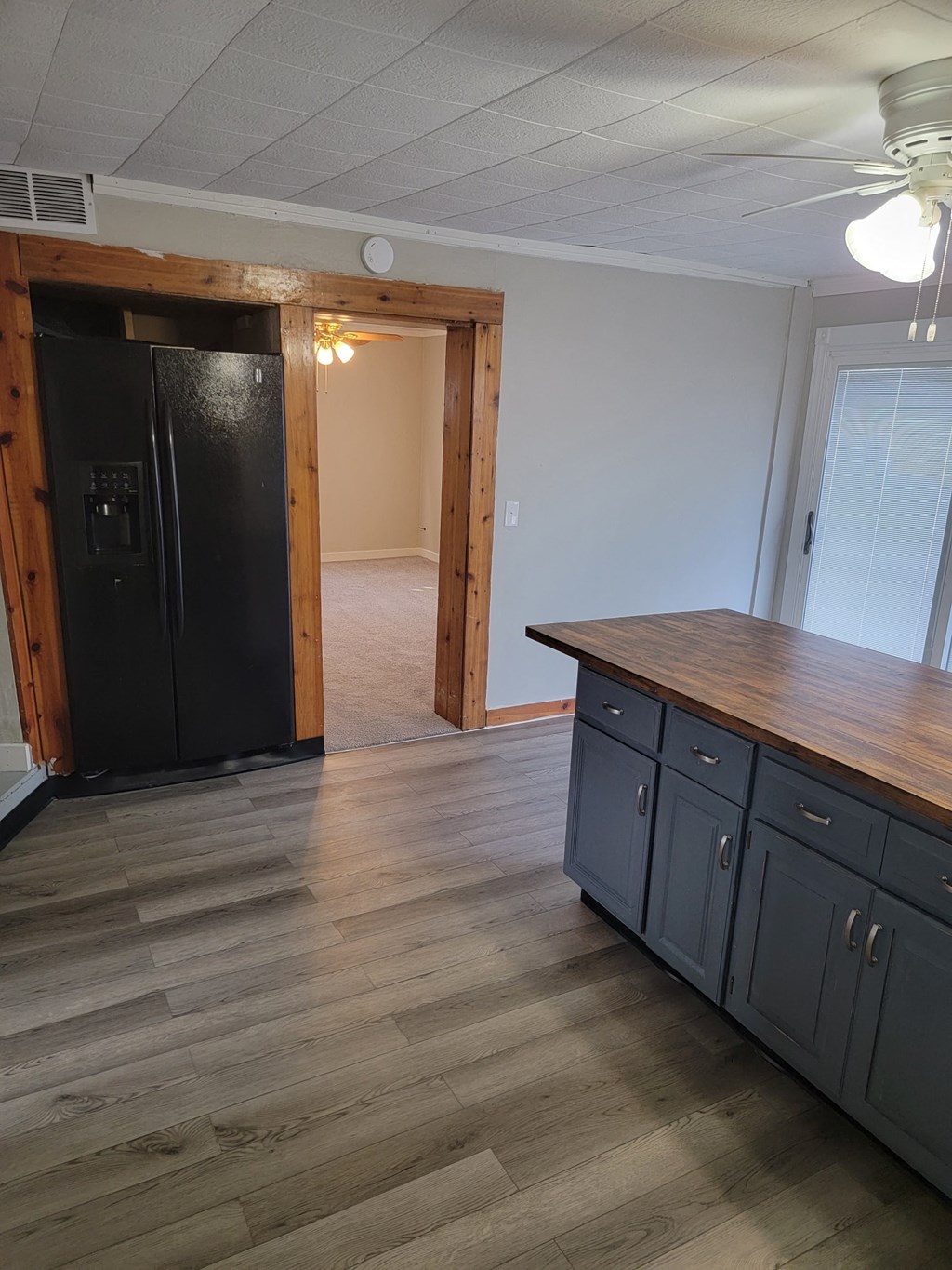 an empty kitchen with a wooden floor and a black refrigerator