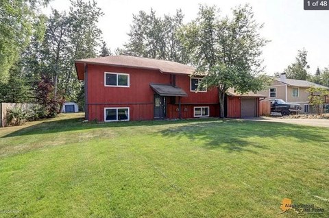 A red house with a black roof and a green lawn in front.