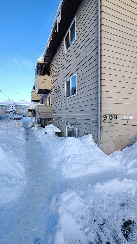 A snow-covered ground in front of a building with the number 909 on it.