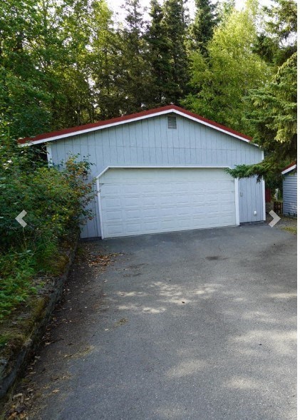 A garage with a white door is surrounded by trees.