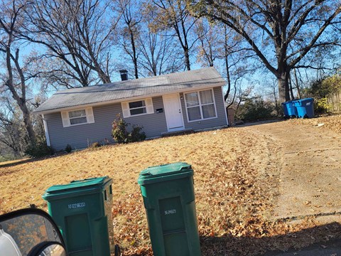a house on a hill with trash cans in front of it