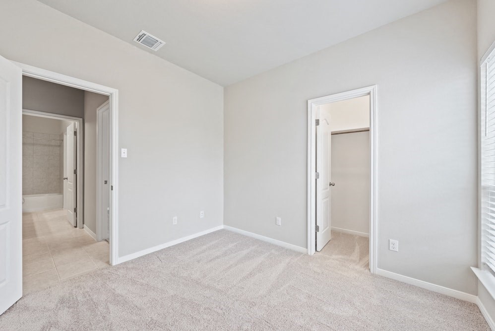 an empty bedroom with doors to the bathroom and a closet