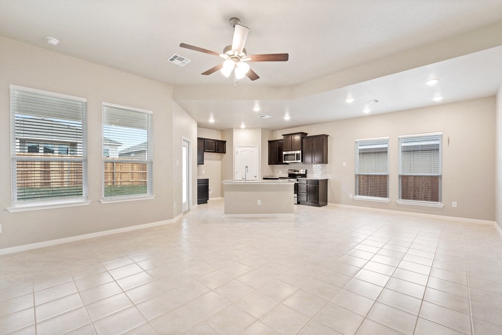 an empty living room with a kitchen and a ceiling fan