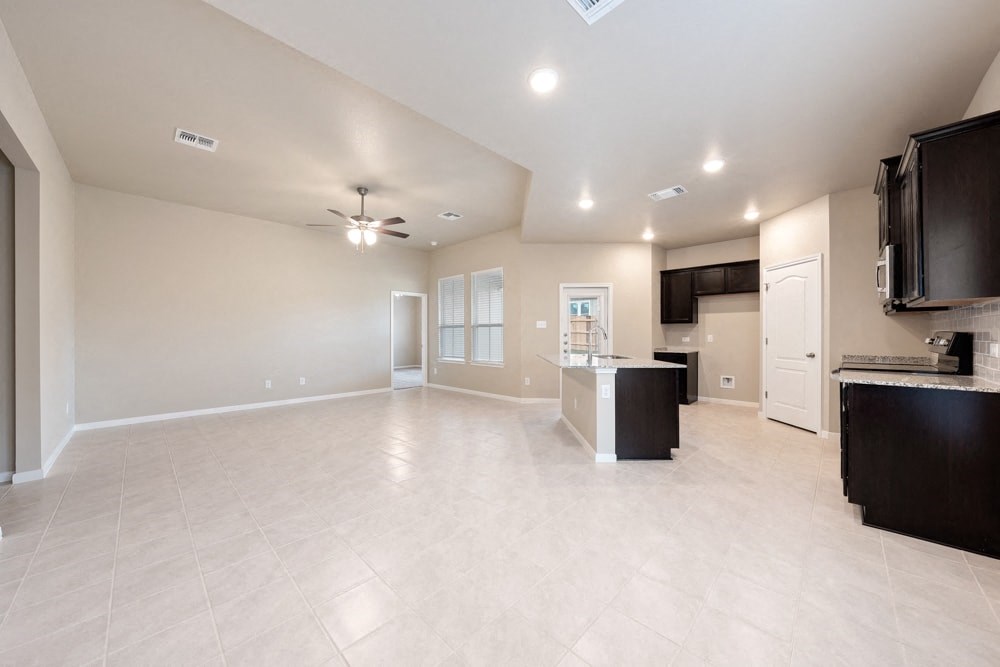 an empty living room with a kitchen and a ceiling fan
