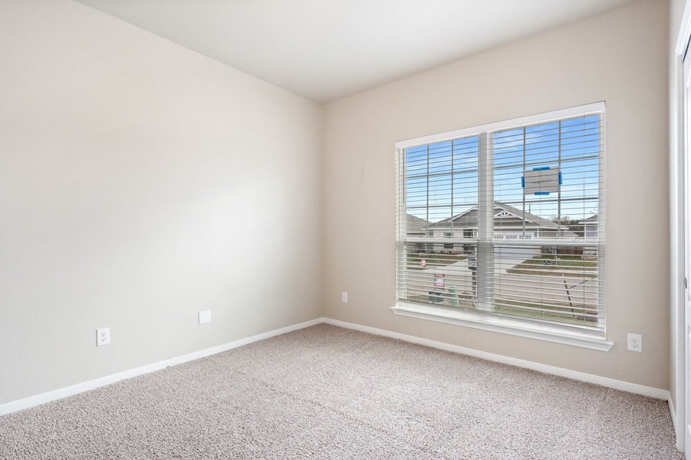 an empty bedroom with a large window and carpeting