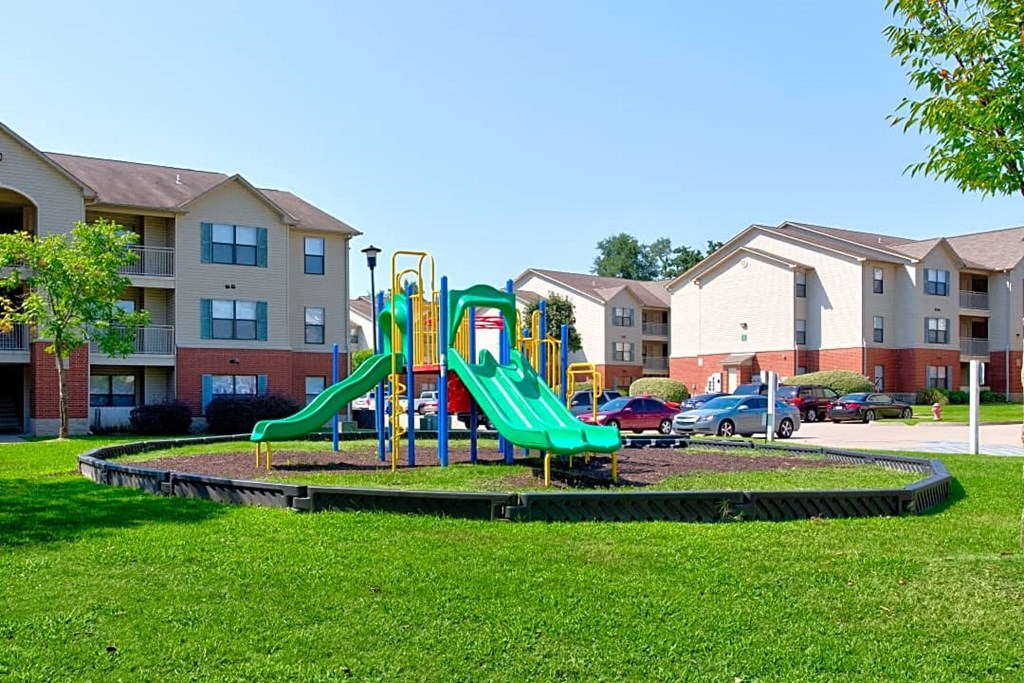 A playground with a green slide in the middle of a grassy area.
