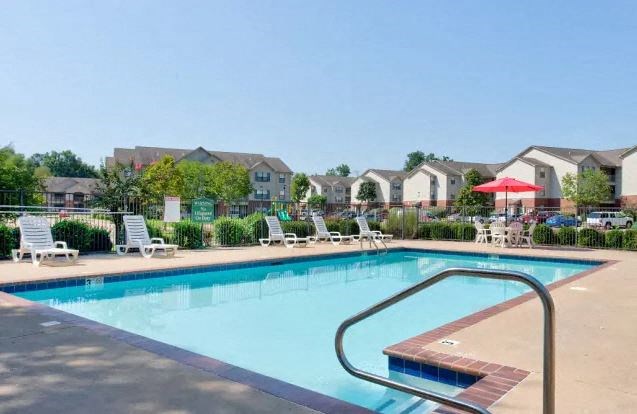 A swimming pool surrounded by lounge chairs and umbrellas with apartment buildings in the background.