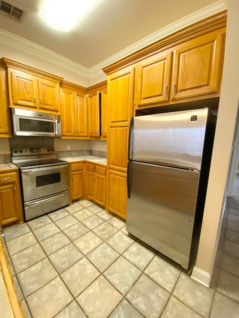 A kitchen with wooden cabinets and a stainless steel refrigerator.