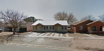 A house with a white roof is surrounded by a concrete wall.