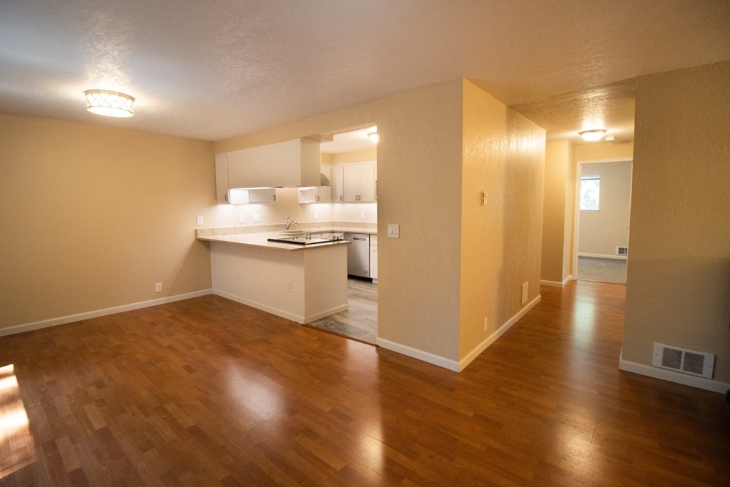 an empty living room and kitchen with a wooden floor