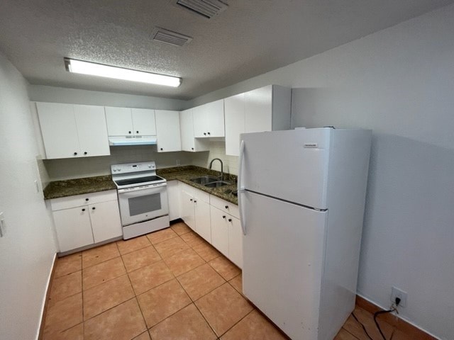A kitchen with white appliances and brown tile flooring.