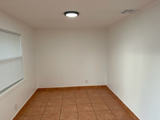 A room with a brown tile floor and a window with blinds.