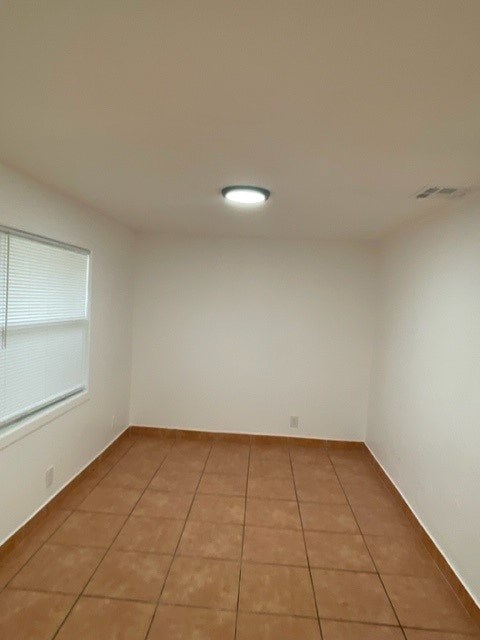 A room with brown tile flooring and a window with blinds.