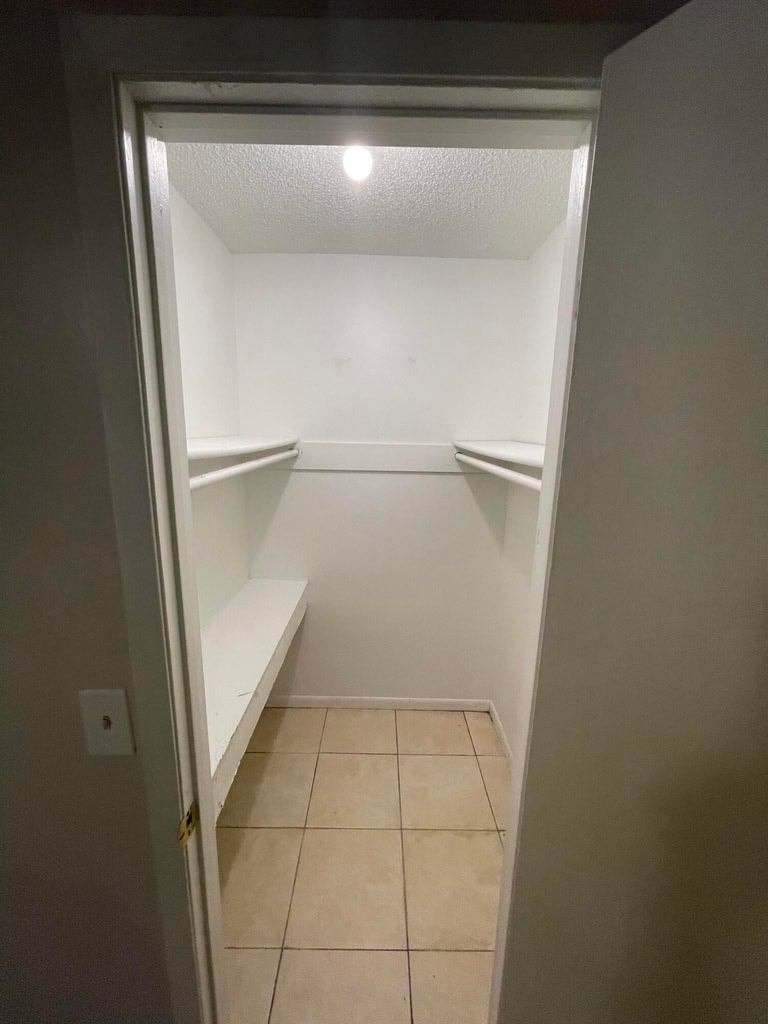 A white door is open to a small pantry with a shelf and a bench.