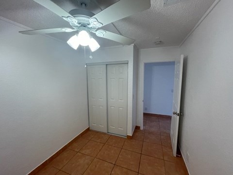 A room with a ceiling fan and a brown tile floor.