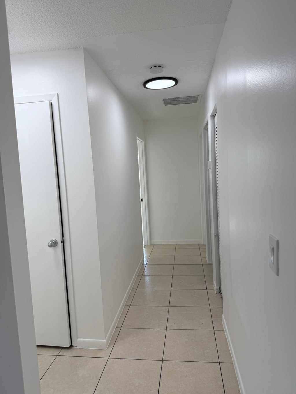 A white hallway with a door on the left and a light on the ceiling.
