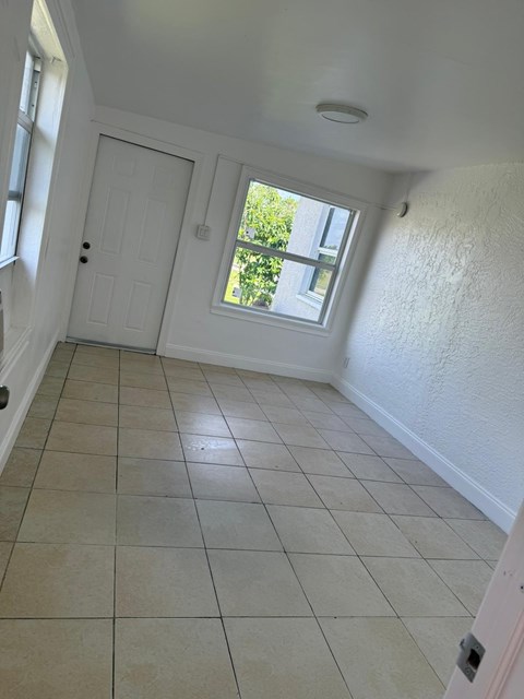 A room with a white door and a window with a view of trees.