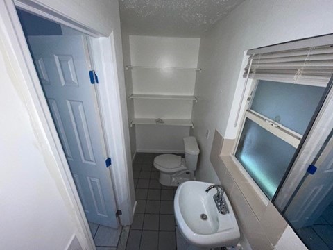 A bathroom with a toilet, sink, and a window.