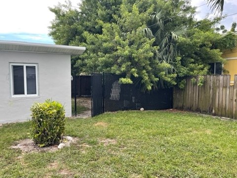 A small white house with a green lawn and a black fence.