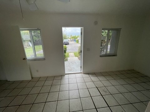 A room with white walls and tiled floor with a doorway leading to a parking lot.