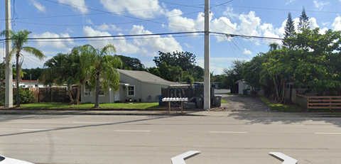 A white house is surrounded by trees and a street.