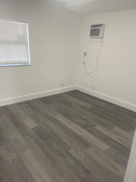 A room with a grey wood floor and a window with blinds.