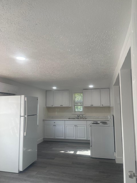 A white refrigerator is in a kitchen with white cabinets.