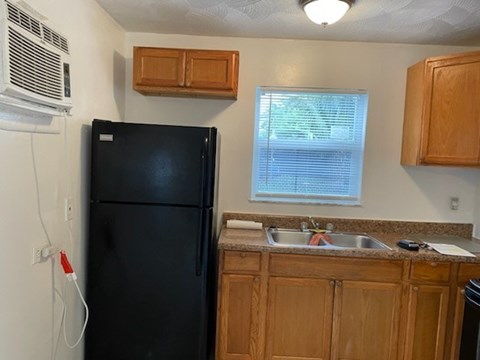 A black refrigerator is in a kitchen with wooden cabinets.