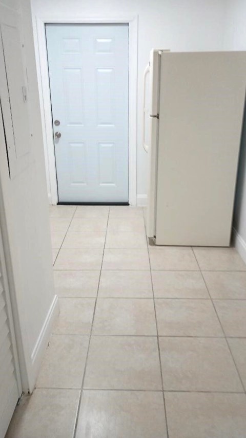 A white door is in a hallway with a white fridge.