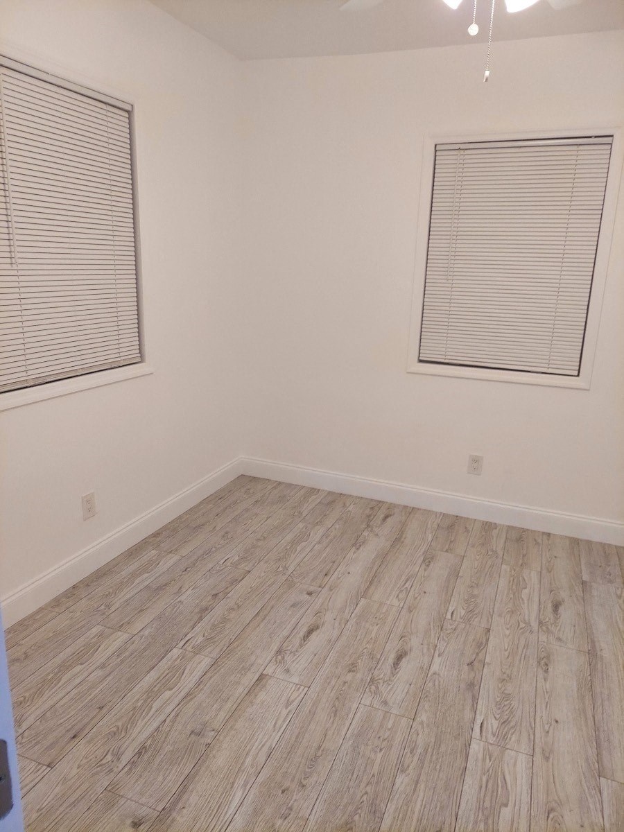 an empty room with wood floors and two windows