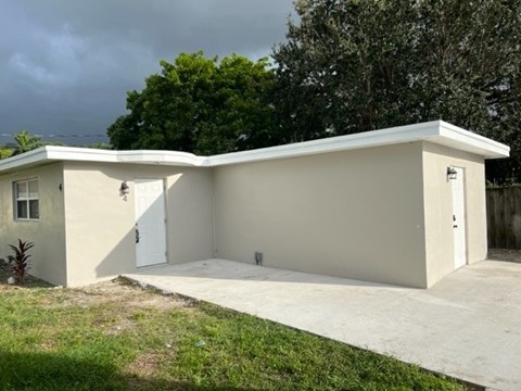 A small white building with a grey roof and a concrete driveway in front.
